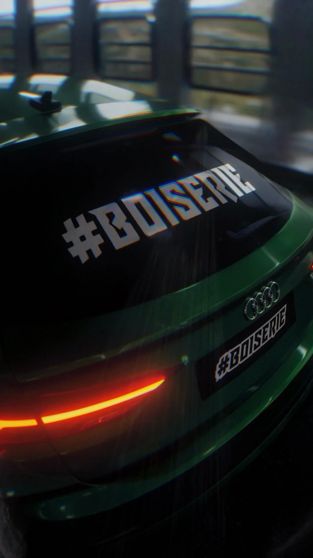 Arrière de l’Audi RS verte, feux allumés et inscription #BOISERIE sur la lunette.
